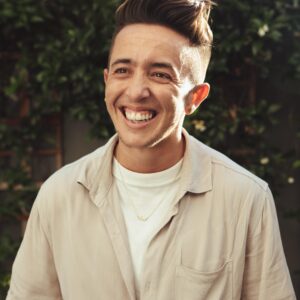transmasculine man smiling against a background of greenery