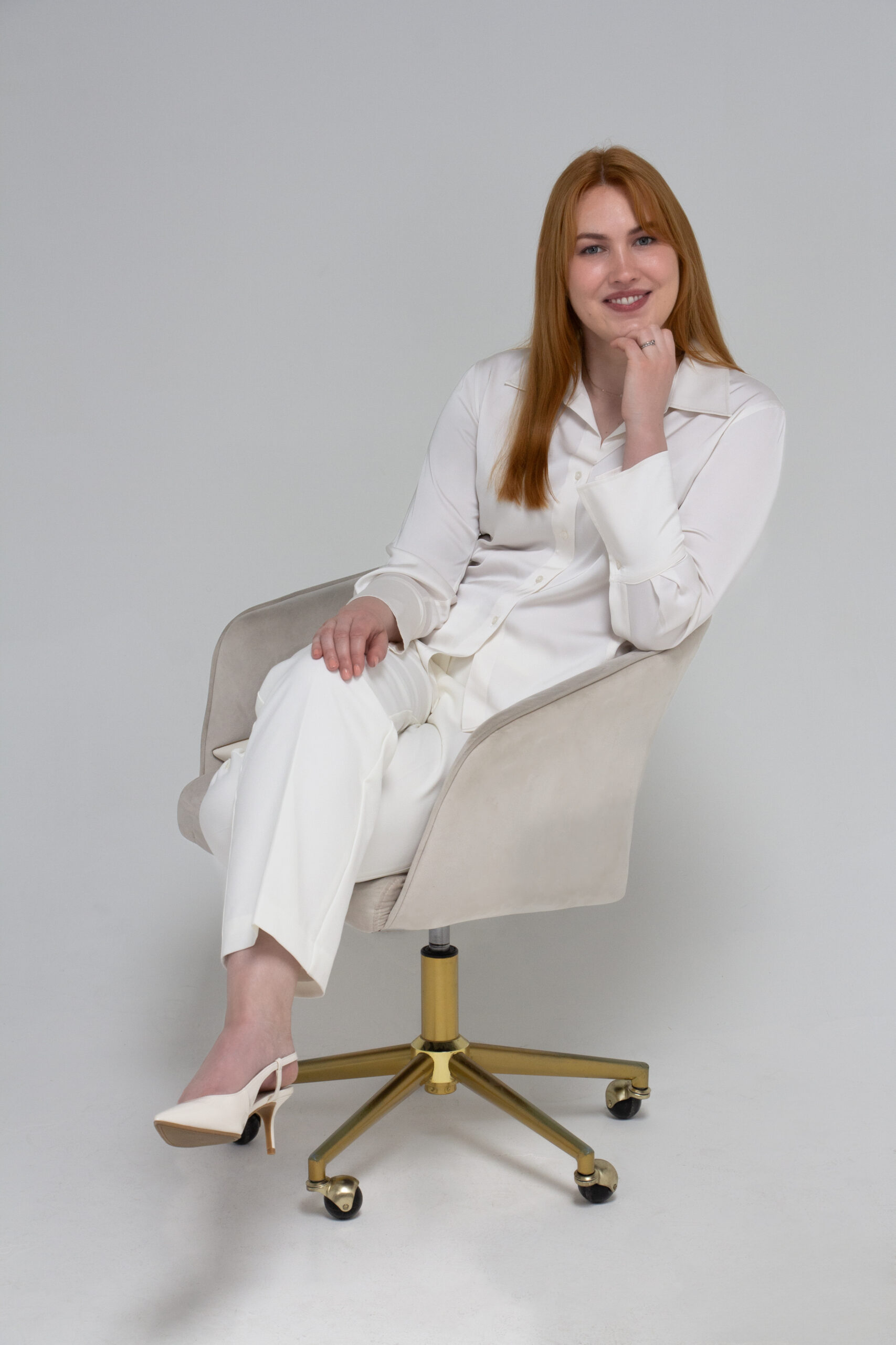 Christy sat on an off-white chair against a white background